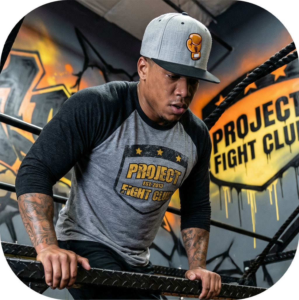 Man wearing a 'Project Fight Club' t-shirt and cap in a boxing ring setting.