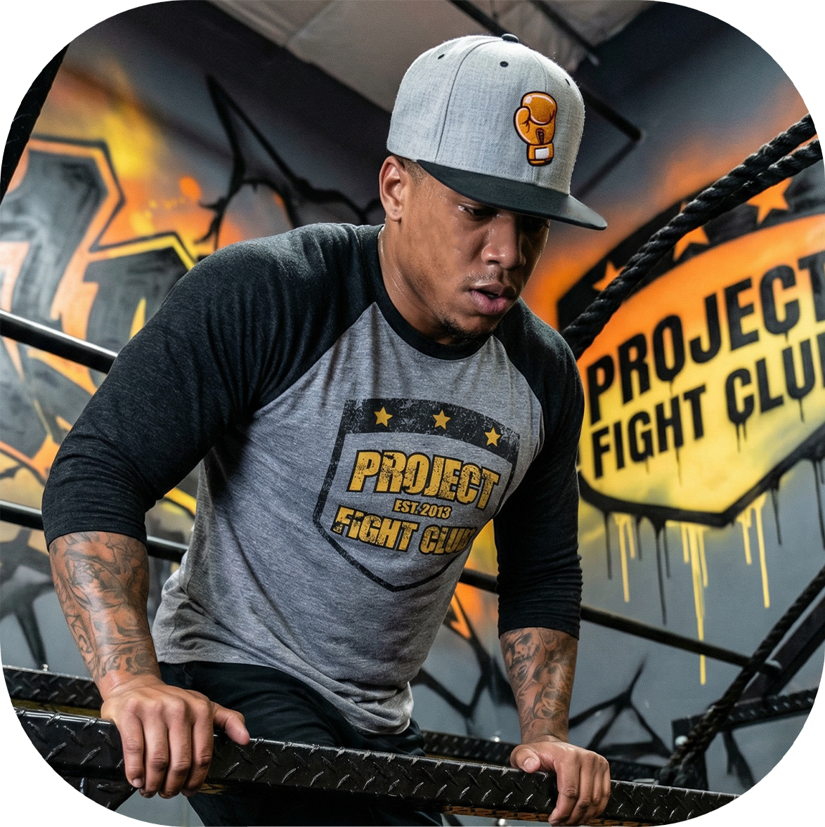 Man wearing a 'Project Fight Club' t-shirt and cap in a boxing ring setting.